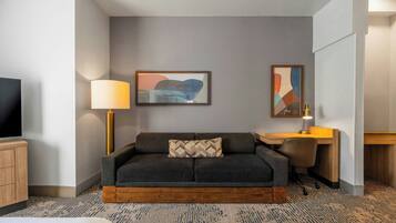 A hotel room with a sofa, a desk, a lamp, and a TV.