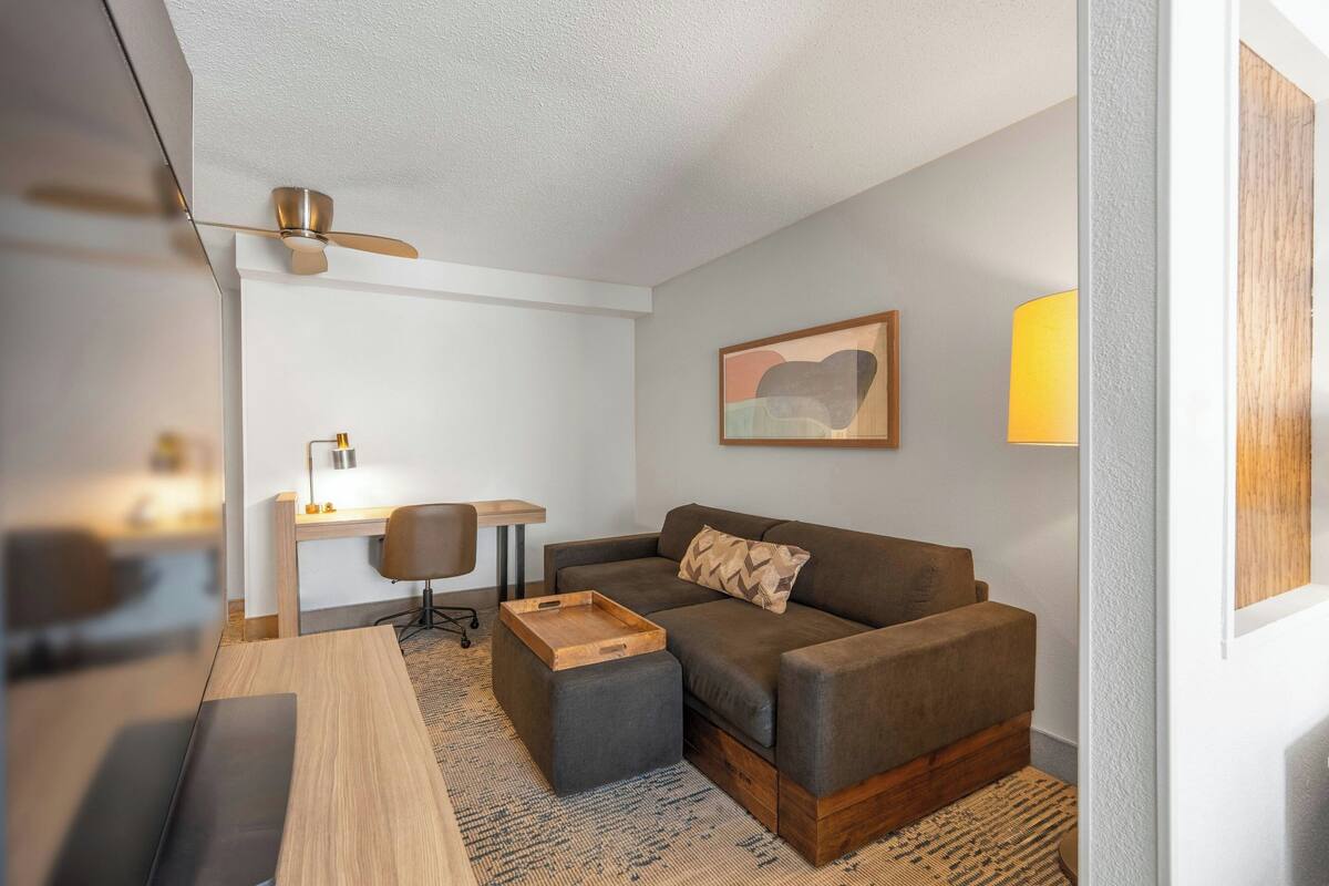 A modern living room with a sofa, a wooden coffee table, a desk with a chair, and a lamp.