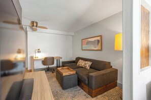 A modern living room with a sofa, a wooden coffee table, a desk with a chair, and a lamp. - SpringHill Suites by Marriott Atlanta Kennesaw (Kennesaw)