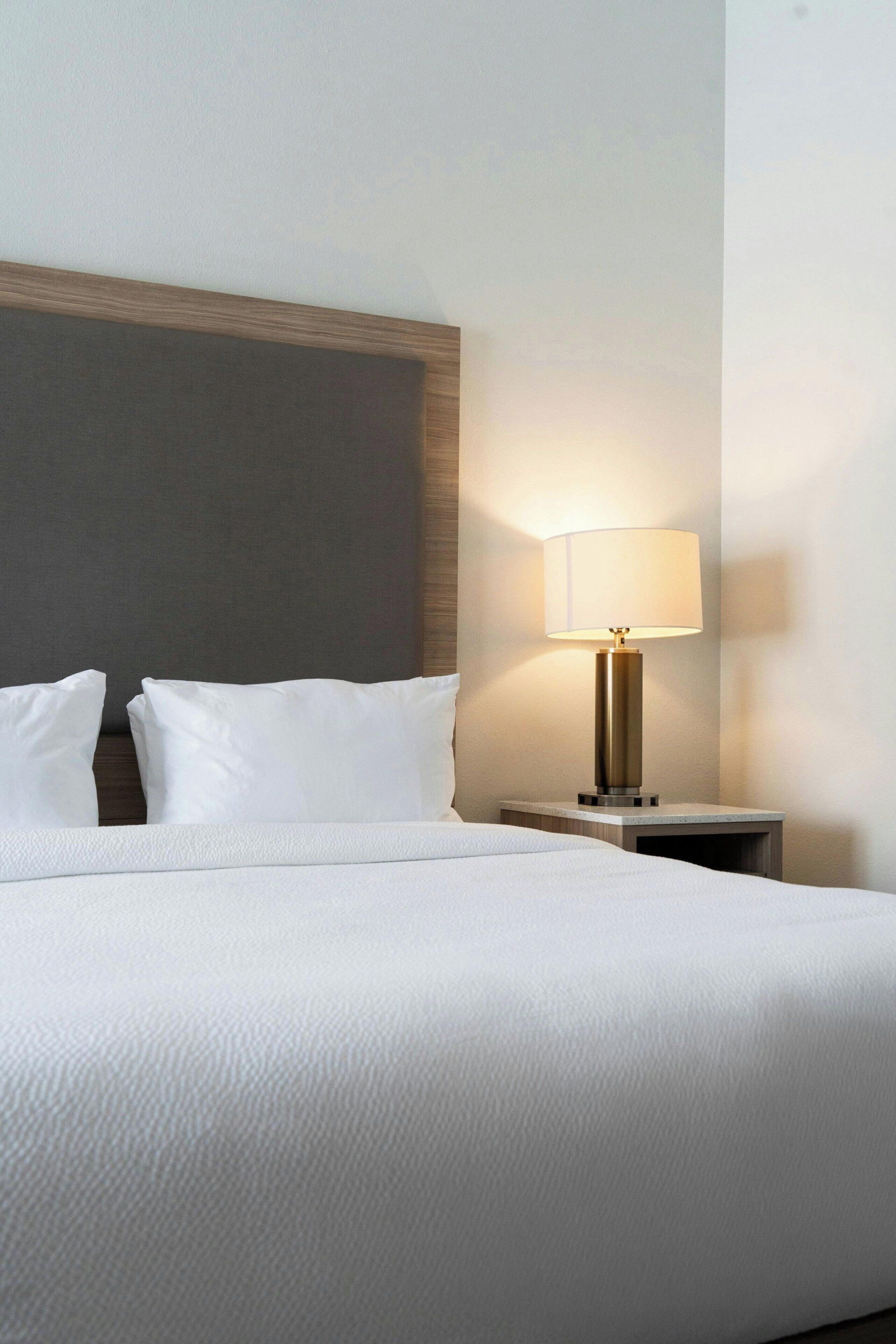 A neatly made bed with white linens, a bedside lamp, and a wooden headboard.