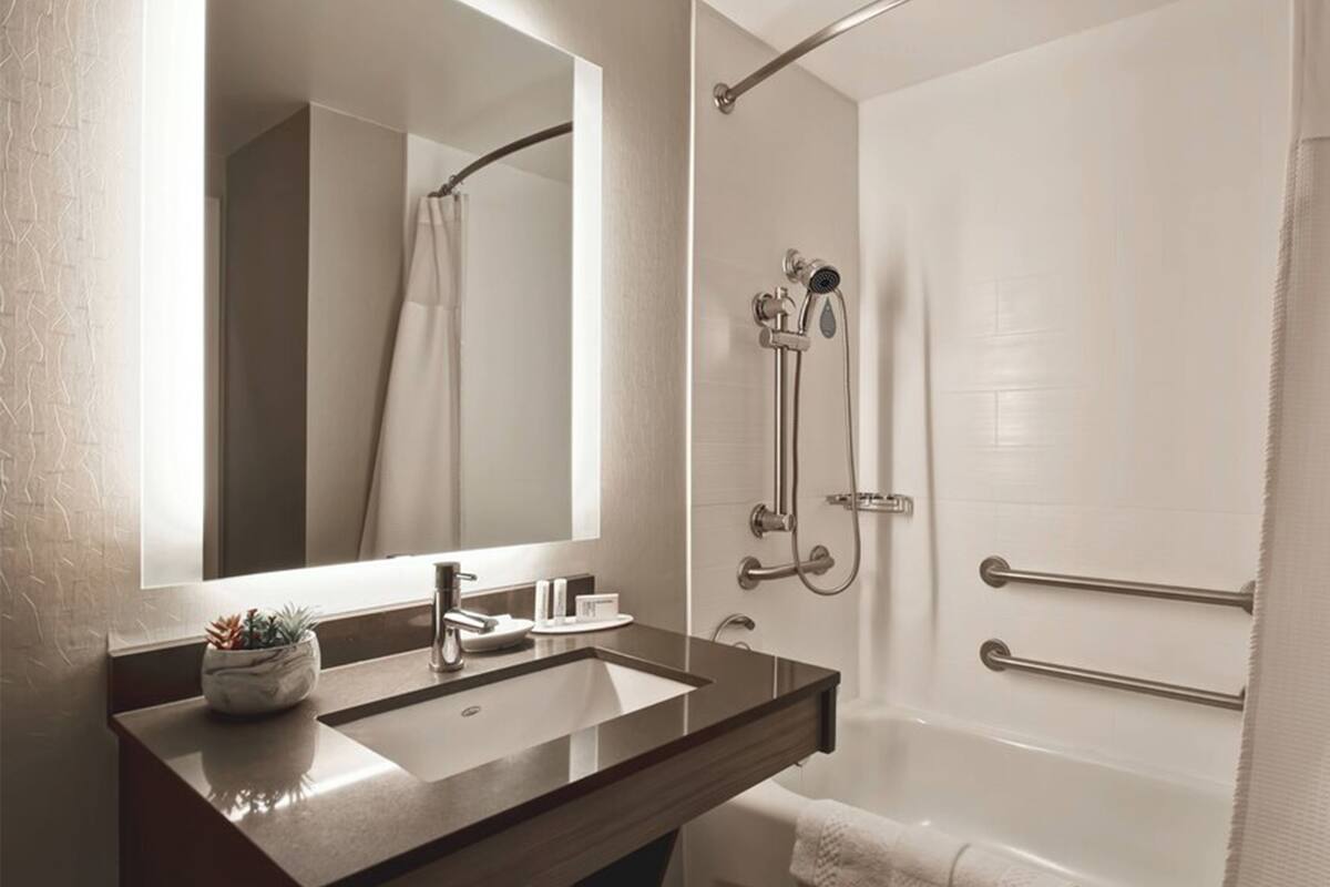 A bathroom with a large mirror, a sink, a shower with a handheld showerhead, and a towel rack.