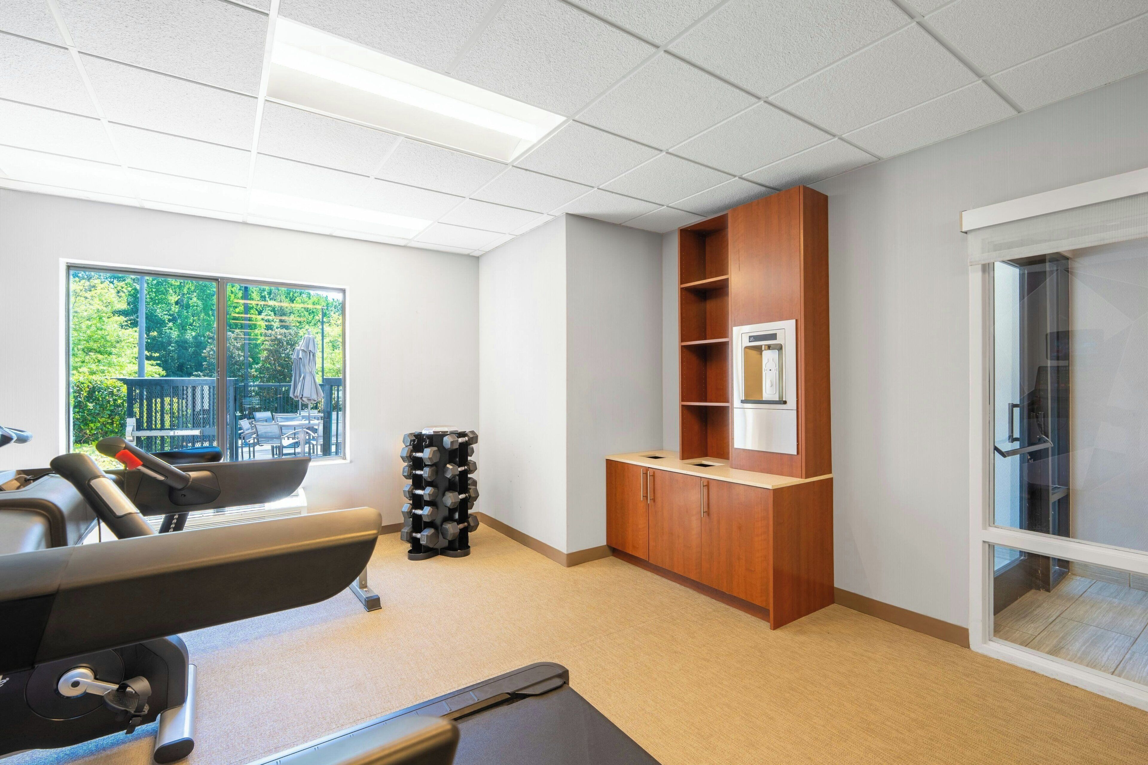 A gym with exercise equipment, a large window, and a wooden cabinet.