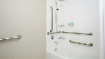 Baño con cabina de ducha, barras de apoyo y pared de azulejos blancos.