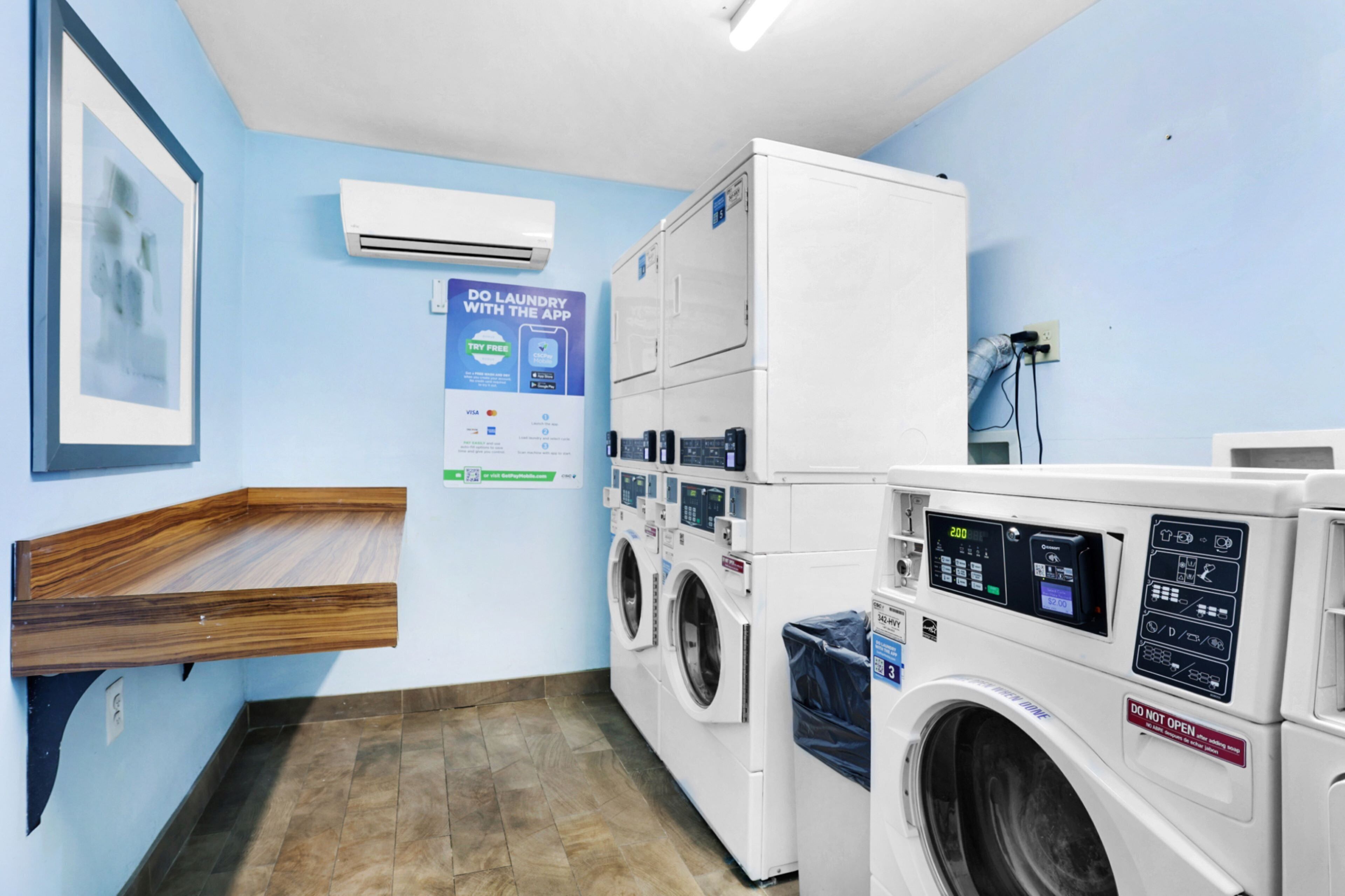 A laundry area with multiple washing machines, a wall-mounted air conditioner, and a poster advertising laundry services.