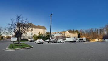 A parking lot with several cars and a white van, surrounded by buildings and a clear sky.