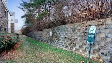 Un muro de piedra con un letrero de estación de desechos de mascotas, un área con césped y un edificio de fachada de piedra.