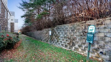 Un muro de piedra con un letrero de estación de desechos de mascotas, un área con césped y un edificio de fachada de piedra.