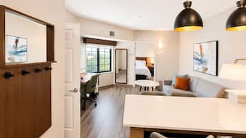 Habitación de hotel con comedor, cama, escritorio y un amplio ventanal.