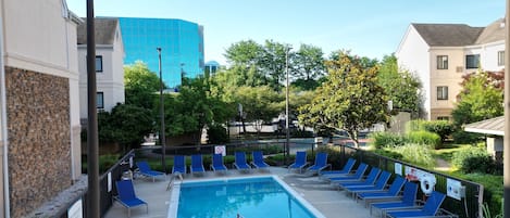 A swimming pool with blue lounge chairs, a diving board, and a no diving sign.