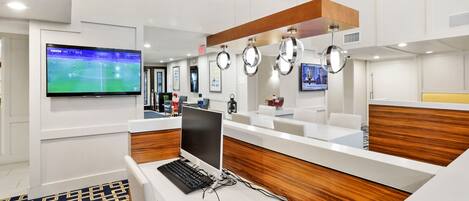 A hotel reception area with a reception desk, a flat-screen TV, a computer, and a wooden accent wall.