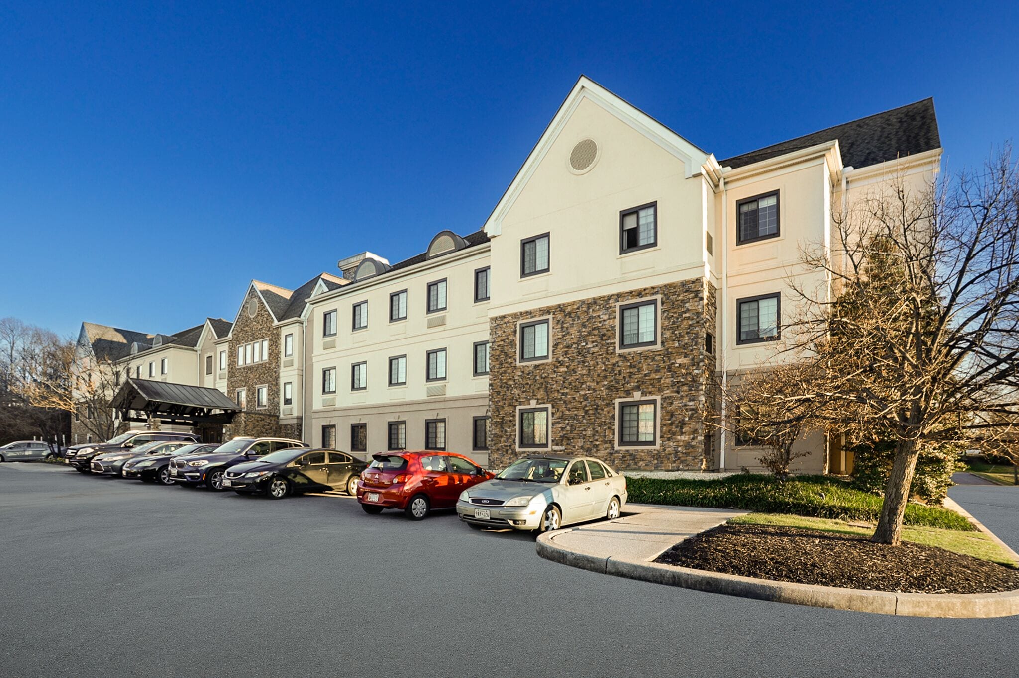A row of modern hotel buildings with a parking lot in front.