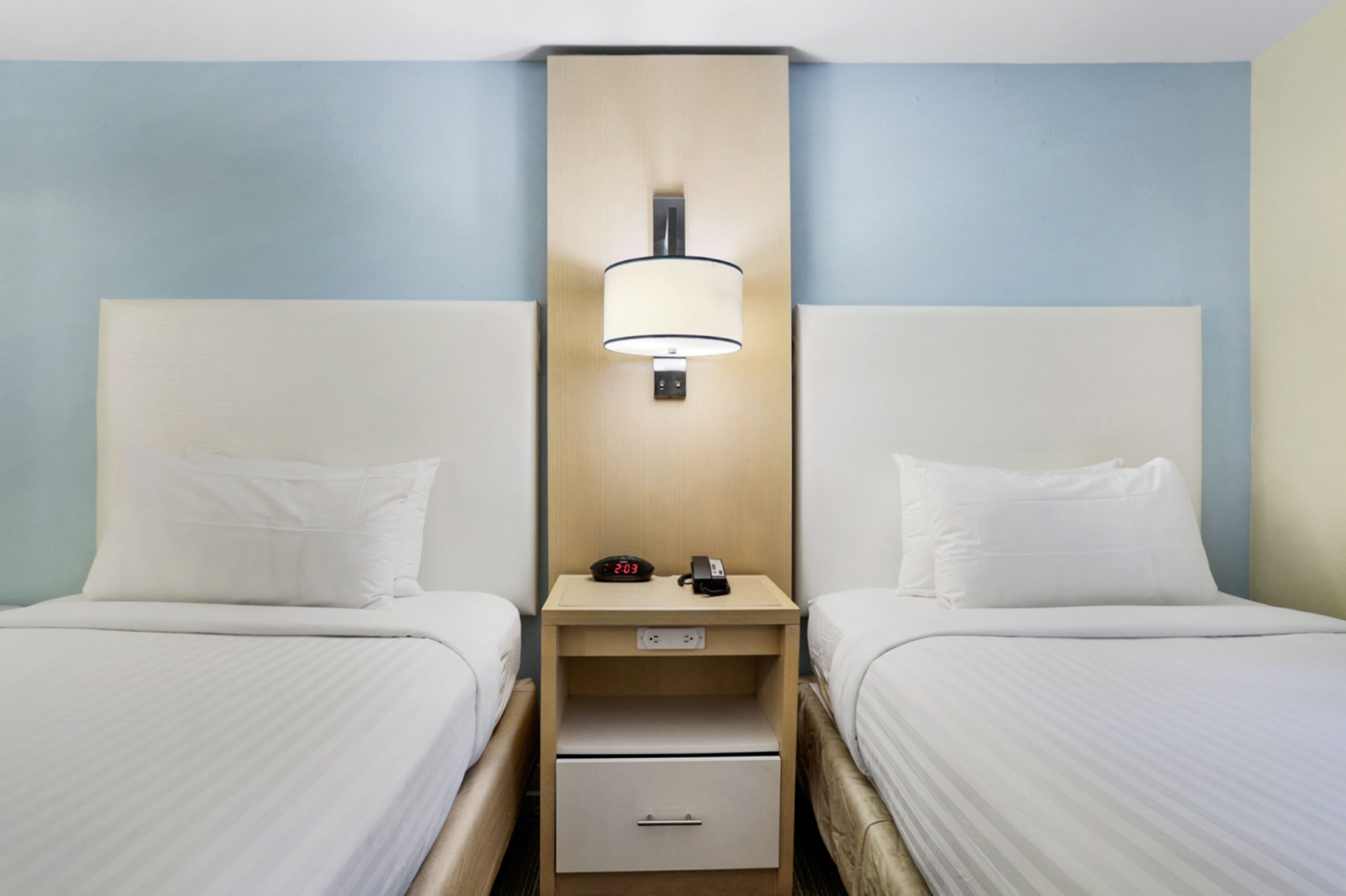 Une chambre d’hôtel avec deux lits, une table de chevet avec une lampe, une horloge et un tiroir.