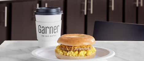 A breakfast sandwich on a plate with a coffee cup labeled 'Garnier' in a modern kitchen setting.