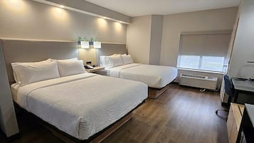A hotel room with two beds, a desk, a chair, a lamp, and a window.