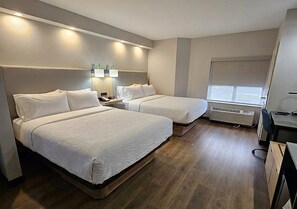 A hotel room with two beds, a desk, a chair, a lamp, and a window.