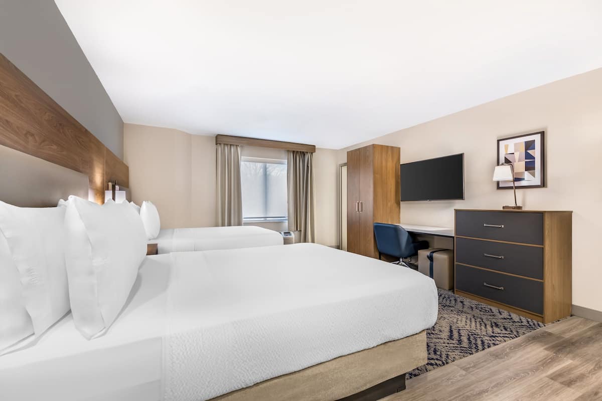 A hotel room with a large bed, a desk, a chair, a TV, and a wardrobe.
