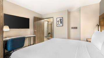A hotel room with a bed, desk, chair, TV, and a door leading to a bathroom.