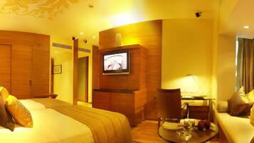 A hotel room with a bed, a TV mounted on the wall, a desk with a chair, and a window with curtains.