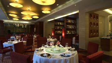 A dining area with round tables set for a meal, red upholstered chairs, and a wall with shelves displaying teapots.