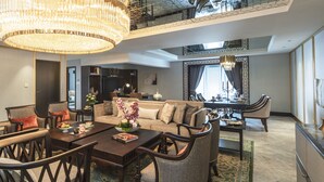 Un vaste salon doté d’un haut plafond, d’un lustre, d’un coin repas avec une table dressée pour quatre personnes, et d’une vue sur l’étage supérieur grâce à une rambarde en verre.
