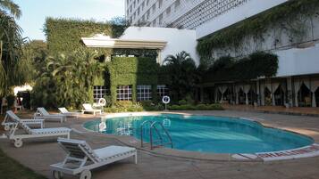 A swimming pool with lounge chairs, a covered area, and a building with a patterned facade.