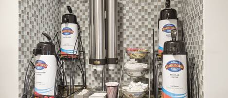 A coffee station with multiple dispensers and a coffee machine, set against a tiled backsplash.