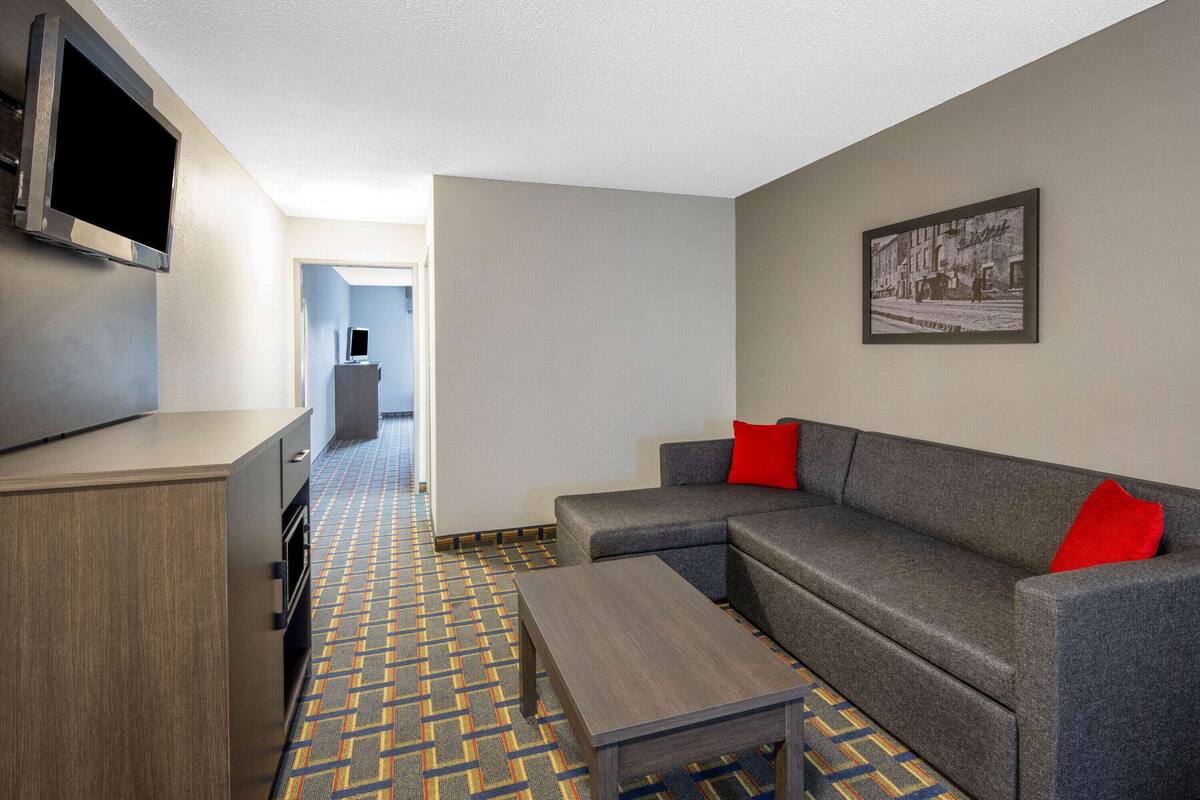 A modern hotel room with a sofa, a coffee table, a flat-screen TV, and a patterned carpet.