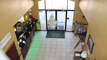 A hotel reception area with a chandelier, a reception desk, and a green mat with the hotel name.