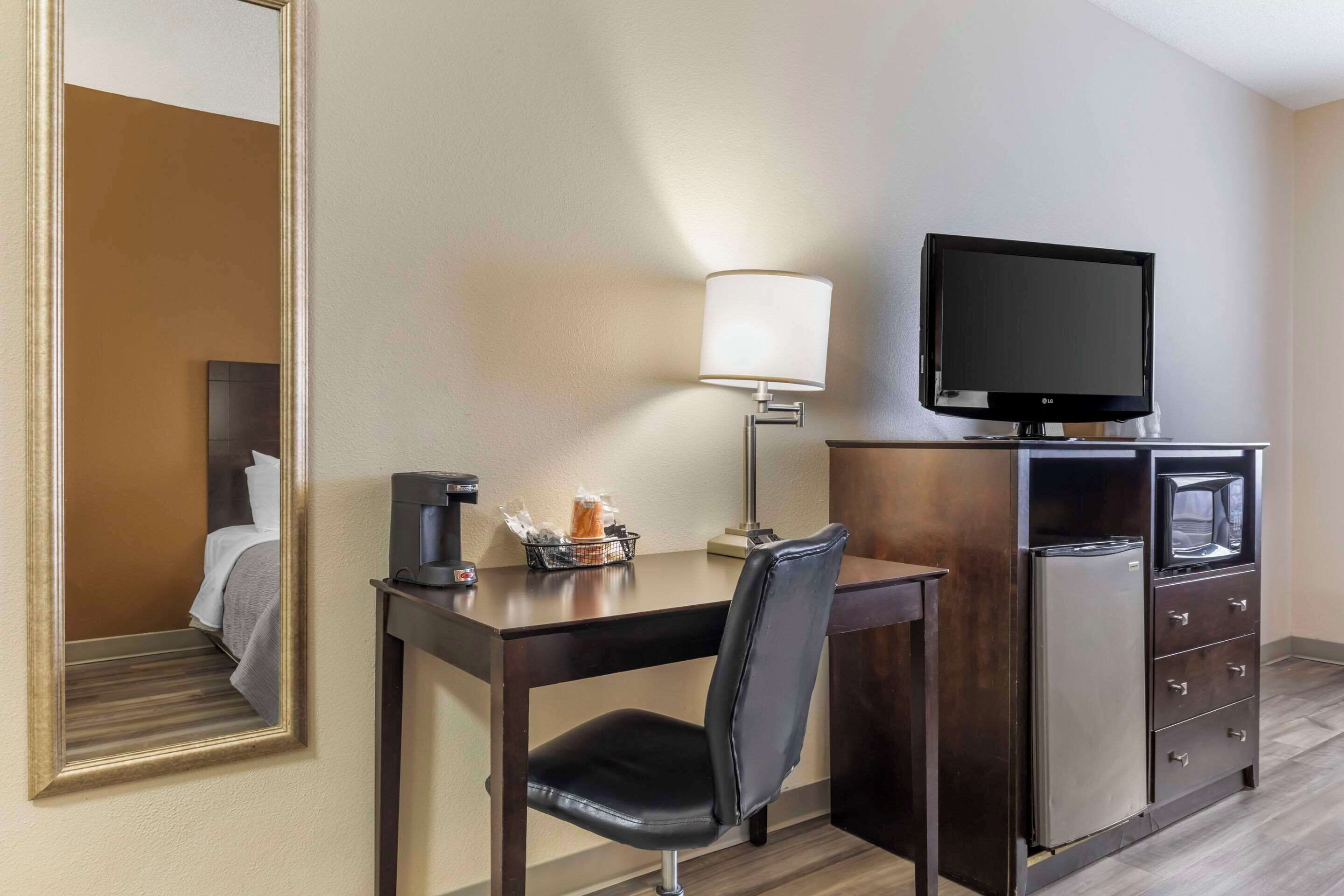 A hotel room with a desk, chair, TV, lamp, and minibar.