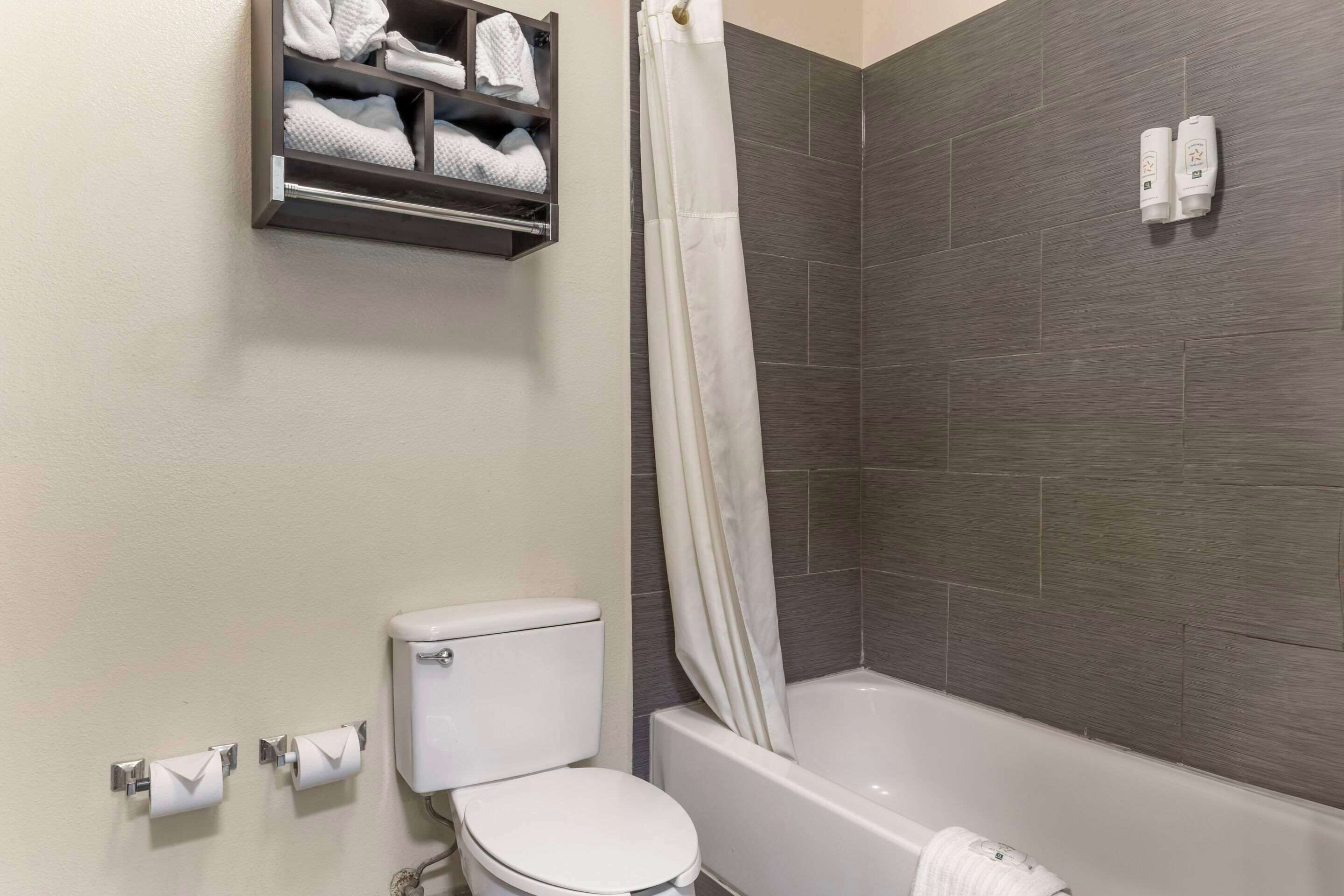 A bathroom with a toilet, a shower curtain, a towel rack with towels, and a toilet paper holder.