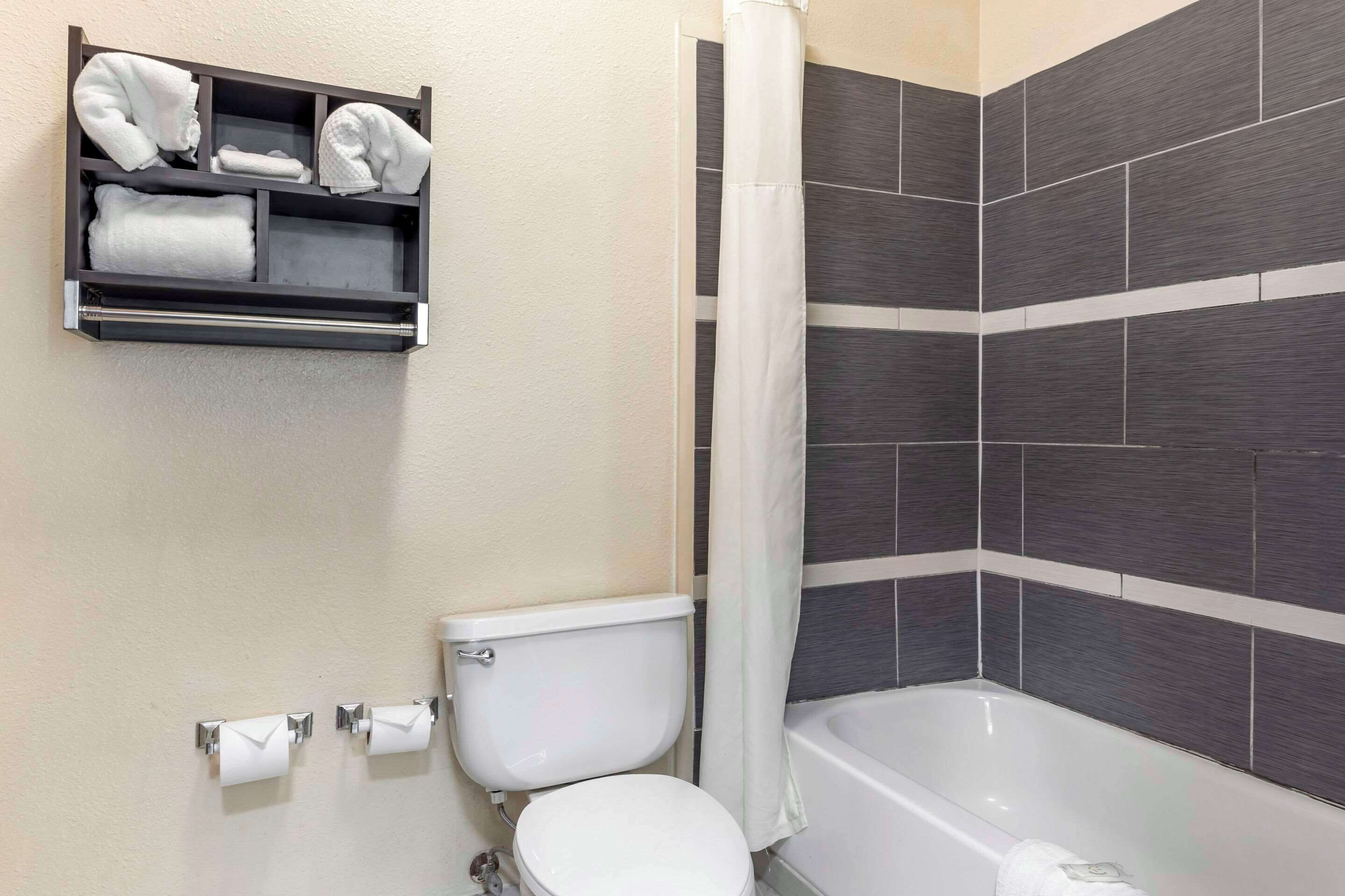 Une salle de bain équipée de toilettes, d’une baignoire, d’un rideau de douche et d’un porte-serviettes avec des serviettes pliées.
