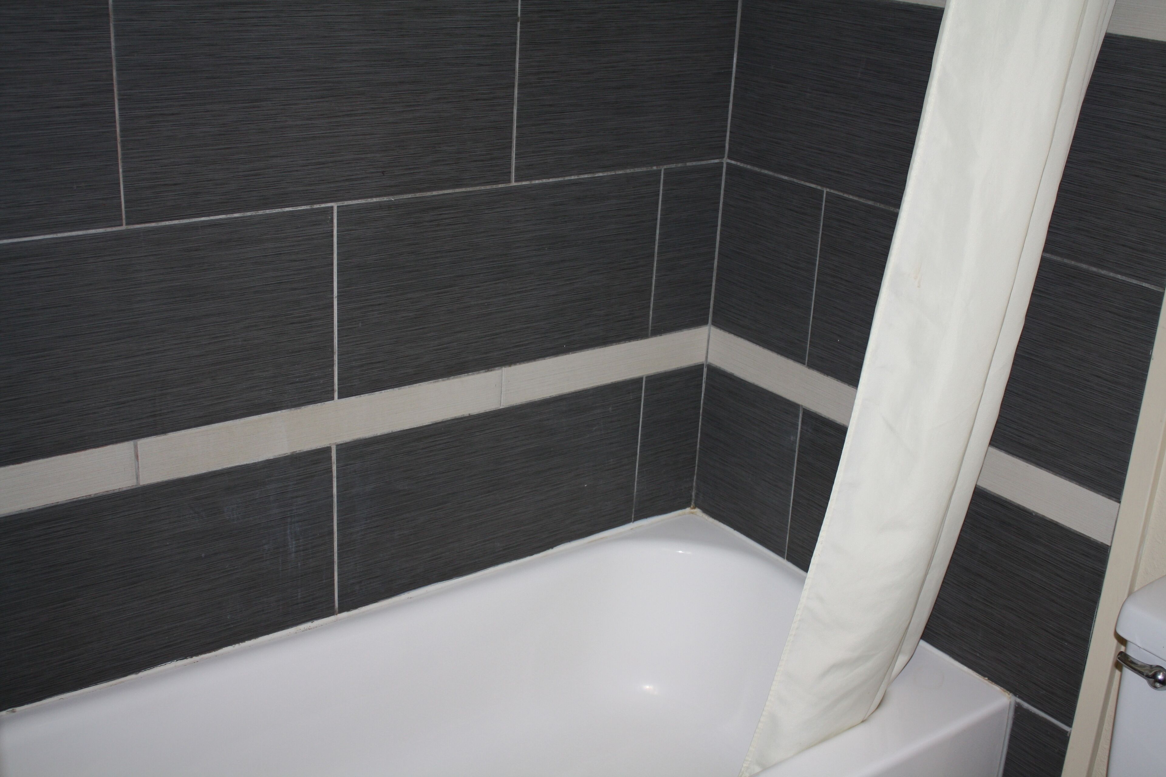 Un baño con una bañera blanca, baldosas gris oscuro y una toalla blanca colgada en la pared.