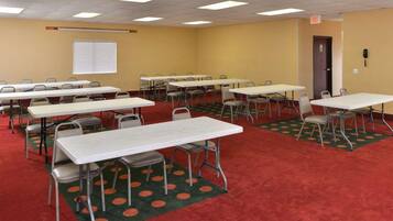 A conference room with multiple tables and chairs, carpeted floor, and ceiling lights.