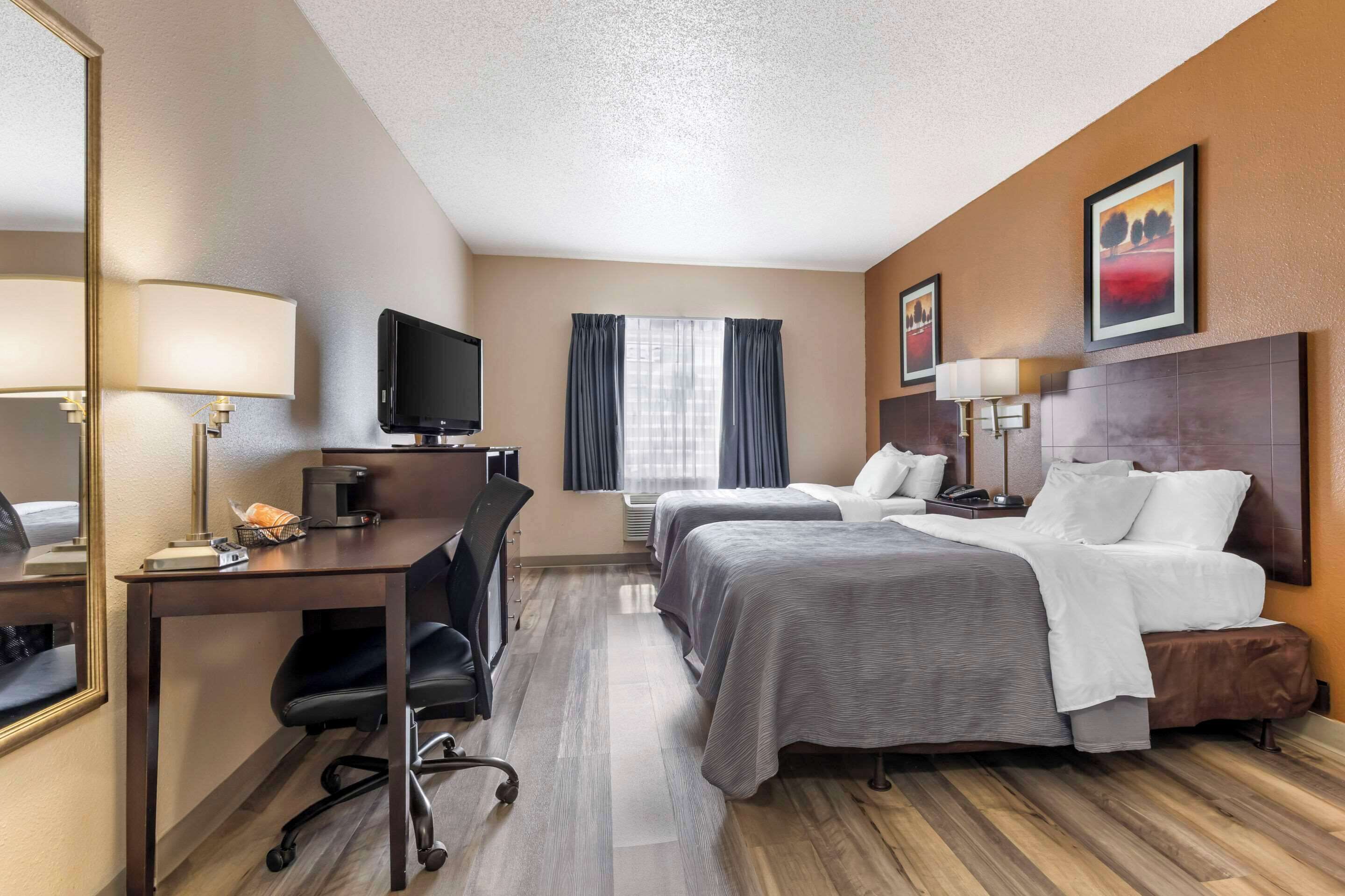 A hotel room with two beds, a desk with a chair, a television, and a window with curtains.