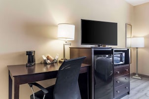 Habitación de hotel con escritorio, televisión de pantalla plana, minibar, cafetera y dos lámparas.