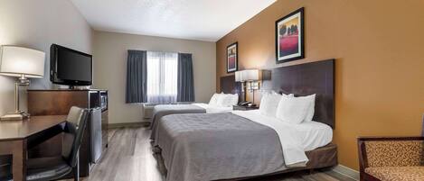 A hotel room with two beds, a desk, a chair, a television, and a window with curtains.