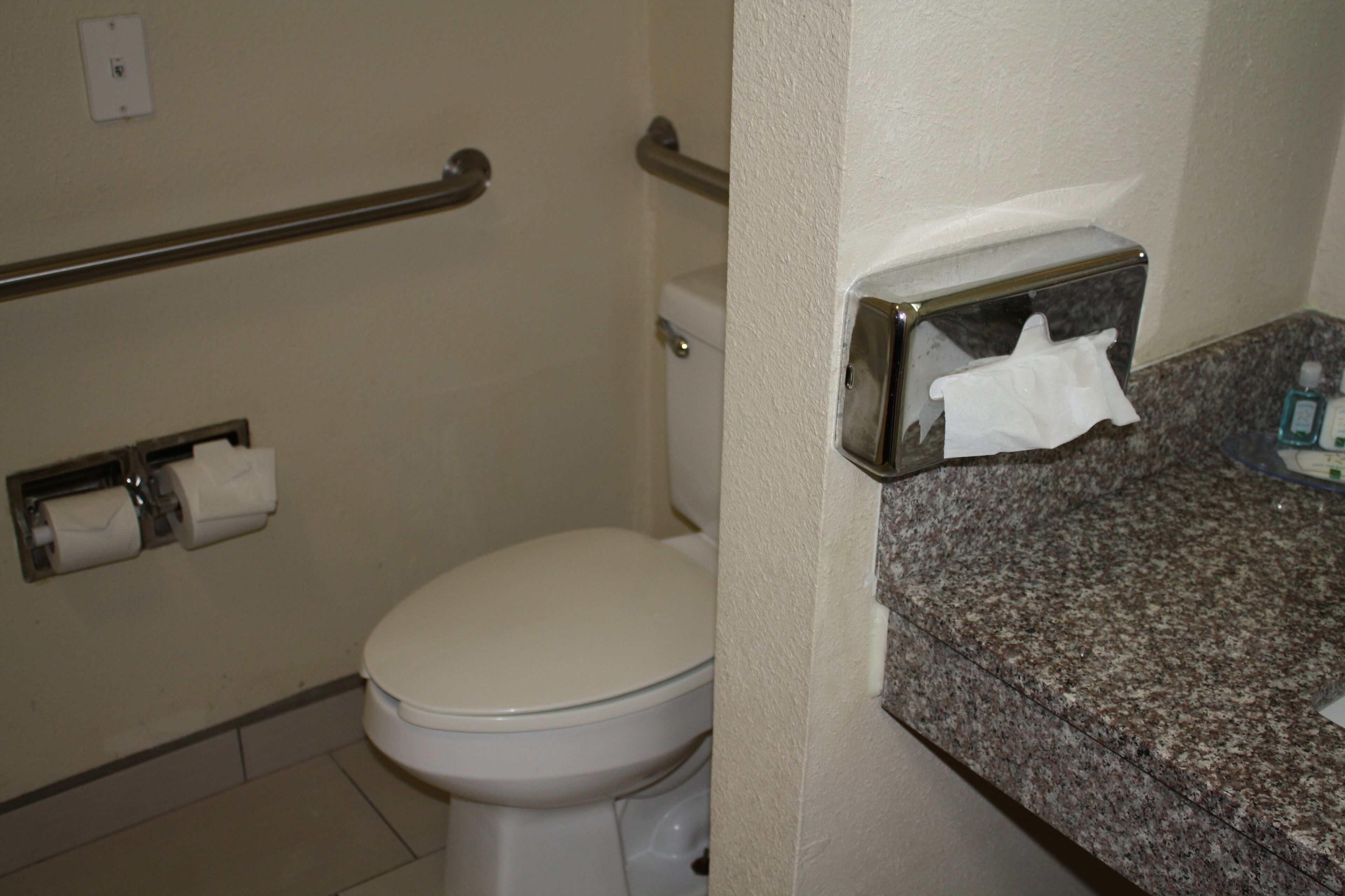 Casa de banho com sanita, dispensador de papel e gel desinfetante para as mãos.