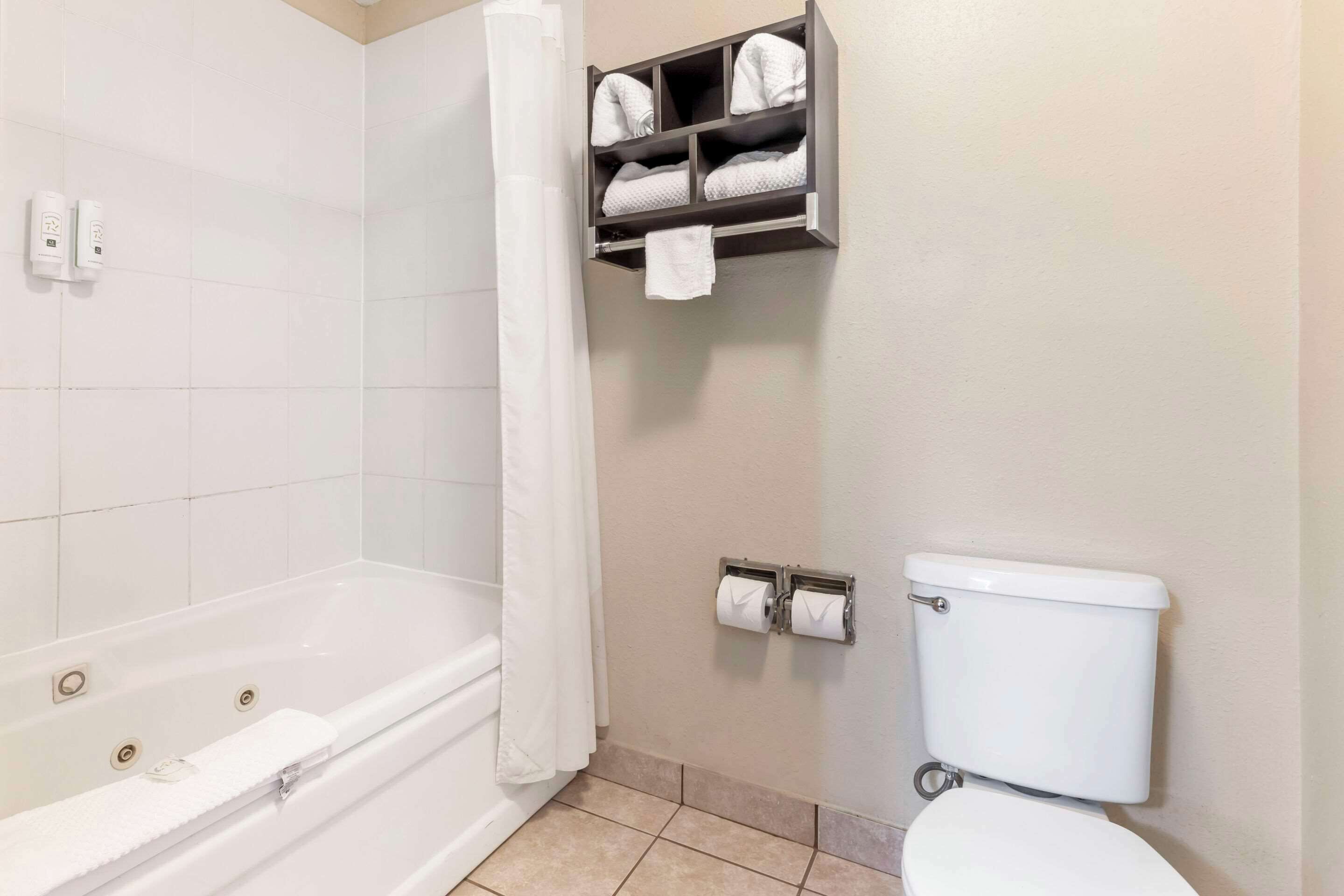 A bathroom with a bathtub, toilet, and towel storage.
