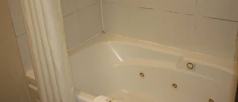A white bathtub with a towel hanging on the side, a shower curtain, and tiled walls.