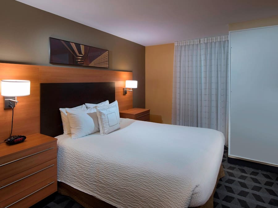 Habitación de hotel con una cama grande, dos mesitas de noche, un televisor de pantalla plana, una obra de arte colgada en la pared y una ventana con cortinas.