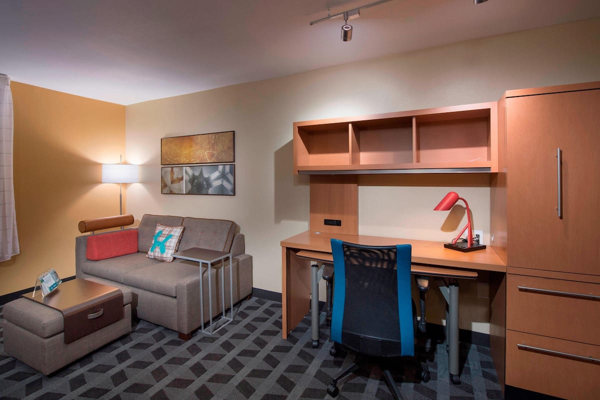 A hotel room with a sofa, a desk, a chair, a lamp, a cabinet, and a small table with a tray.