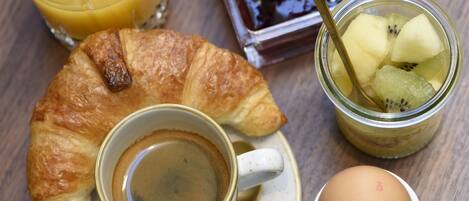 A breakfast setting with a croissant, a cup of coffee, a glass of orange juice, a jar of jam, and a boiled egg on a wooden table.
