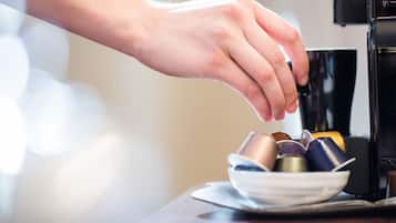 A hand reaching for a coffee cup from a stack of cups on a table next to a coffee machine.