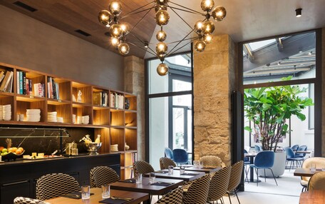 A modern dining area with a wooden ceiling, a central chandelier, and a bookshelf filled with books and kitchenware.