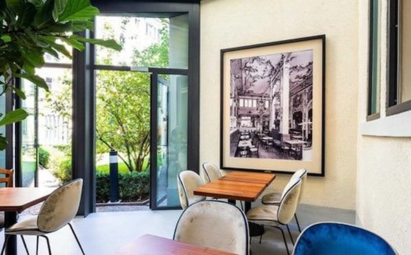 Un comedor moderno con un amplio ventanal, una fotografía histórica enmarcada y una mezcla de sillas de metal y tapicería.