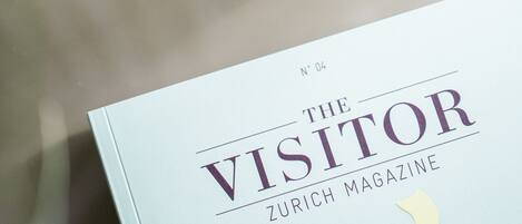 A book titled "The Visitor" with a glass of water and a plant on a table.