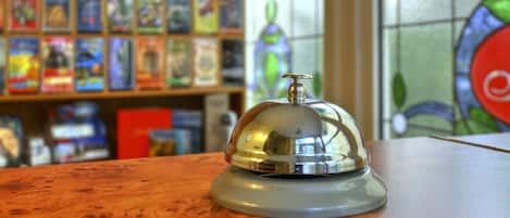A hotel reception area with a wooden counter, a bell, and a stained glass window in the background.