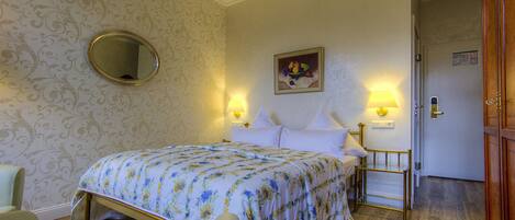 A hotel room with a bed, a round mirror, a painting, two bedside lamps, and a door.