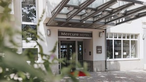 The exterior of the Mercure Hotel with a modern entrance, glass doors, and a sign indicating its location in Magdeburg.