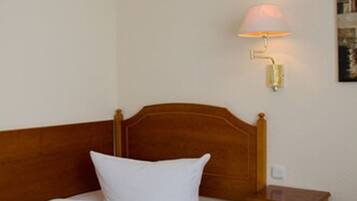 Una cama bien hecha con sábanas y almohadas blancas, un cabecero de madera, una mesita de noche con una lámpara y un cuadro en la pared.